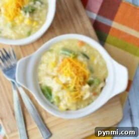 A bowl of creamy pressure cooker chicken and rice soup topped with shredded cheese sits next to two forks on a wooden board.