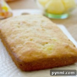 Freshly baked pineapple bread loaf on a white plate, reminiscent of delicious banana pineapple muffins, with a bowl of pineapple chunks in the background.