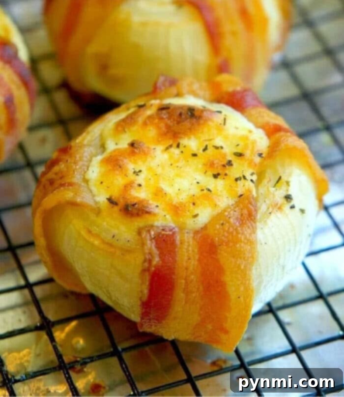 Close-up of golden brown mozzarella stuffed bacon-wrapped onions, showcasing the melted cheese and crispy bacon, resting on a cooling rack.