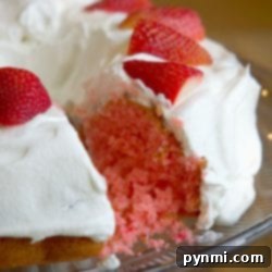 A delightful 2 ingredient strawberry cake with white frosting and sliced strawberries adorning the top, elegantly presented on a glass plate.