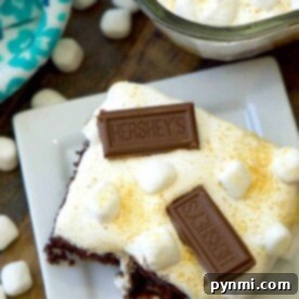 A delicious s'mores poke cake, adorned with marshmallows and Hershey bars, sits elegantly on a white plate.