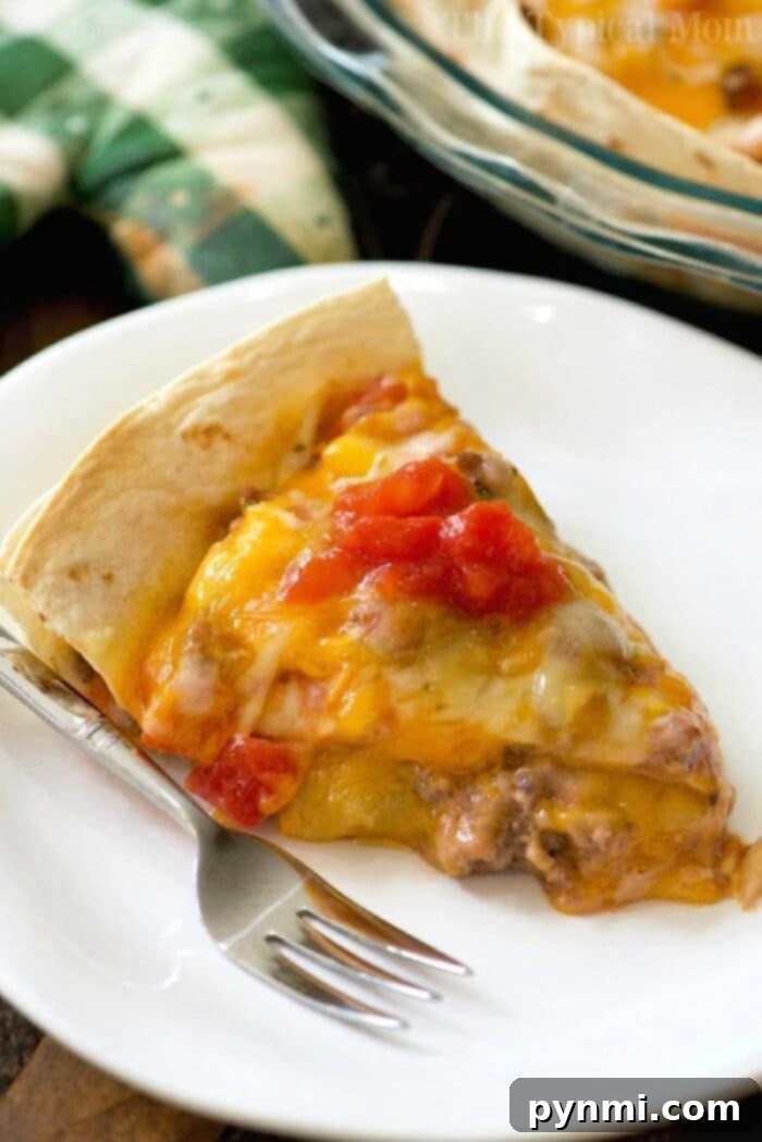 A slice of Copycat Taco Bell Mexican Pizza on a white plate with a fork, reminiscent of a Taco Bell Mexican Pizza, topped with melted cheese and diced tomatoes.