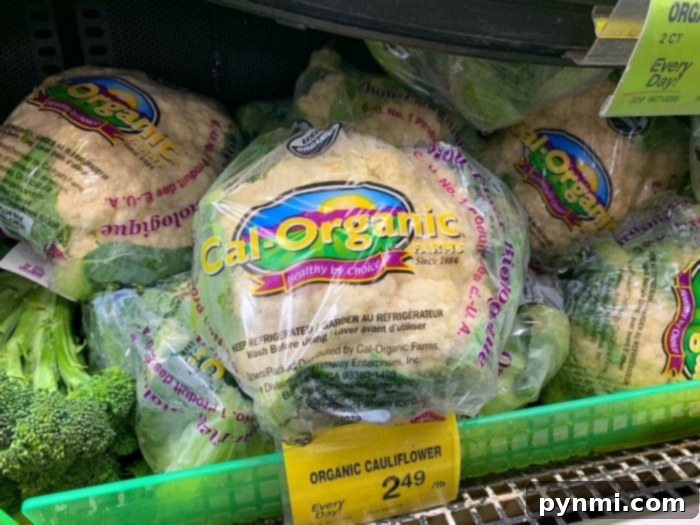 Crispy Roasted Brussels Sprouts and Cauliflower 2 Packages of Cal-Organic Farms organic cauliflower are displayed in a grocery store, perfect for your next air fryer cauliflower recipe. Each one is wrapped in branded plastic packaging, with a price tag showing $2.49 per pound. Broccoli is partially visible in the display.