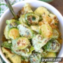 Bowl of roasted Brussels sprouts and cauliflower coated in green sauce, served over hearty grains with a fork—perfect for fans of Roasted Brussel Sprouts and Cauliflower.
