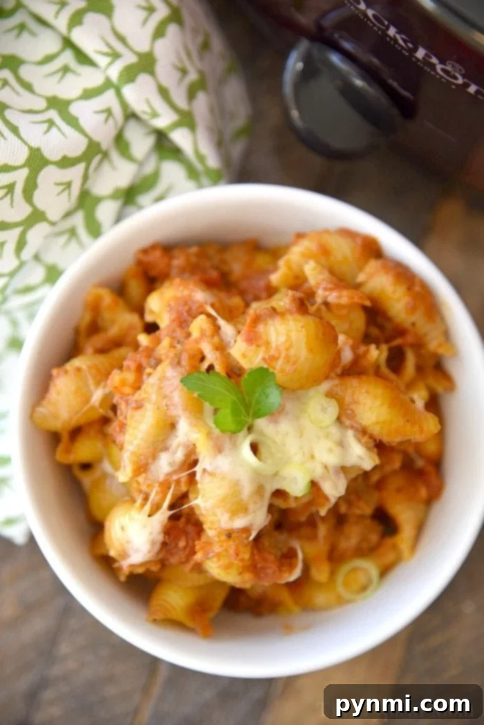 A bubbling crockpot filled with deconstructed lasagna casserole, showing melted cheese and rich tomato sauce with pasta.