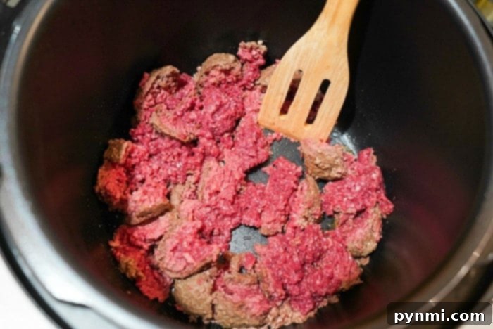 Cooked ground beef with diced onions in a pan, ready to be added to the crockpot for lasagna casserole.