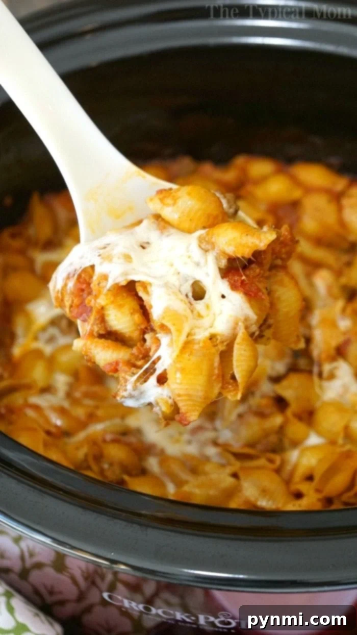 A spoonful of cheesy pasta and sauce is being lifted from a crockpot lasagna, showcasing the delicious layers within.