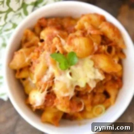 A bowl of crockpot lasagna, is garnished with green herbs and sits on a wooden table with a patterned cloth nearby.