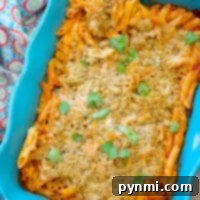 Baked penne pasta in a blue dish topped with breadcrumbs and garnish, with a colorful cloth beside it, becomes an effortless delight in this no-boil chicken parmesan casserole.