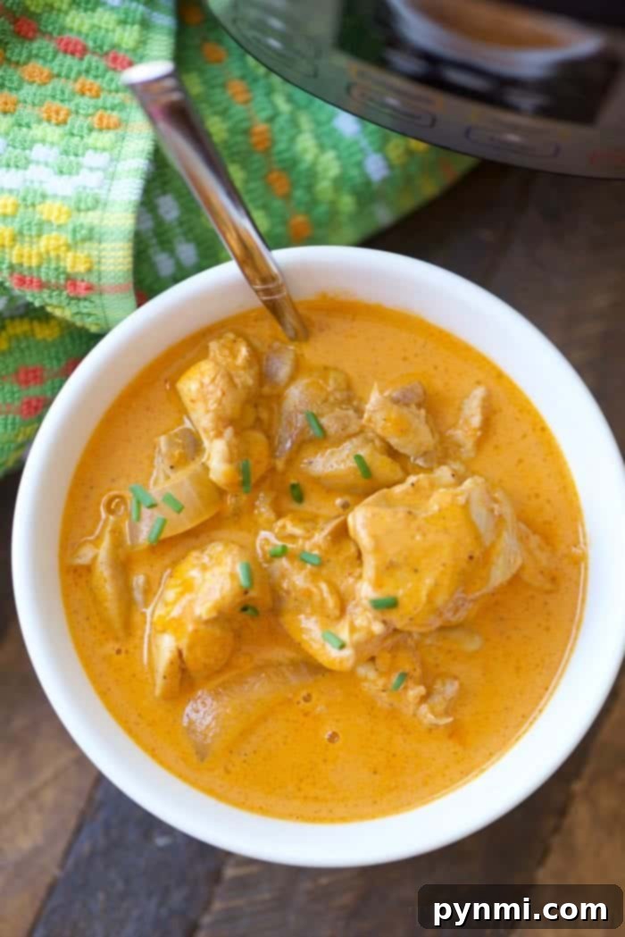 A bowl of creamy chicken curry, one of those easy instant pot chicken recipes, garnished with herbs. A spoon and a colorful cloth sit nearby, ready for a delightful meal experience.