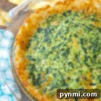 A tater tot spinach quiche sits invitingly in a glass pie dish on a wooden table, surrounded by a cheerful yellow cloth and a vibrant blue napkin.