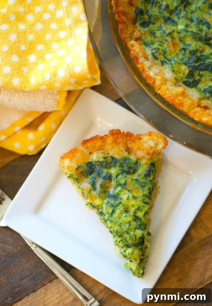 Slice of tater tot crusted spinach quiche on a white plate with a fork