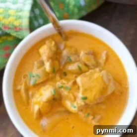 A bowl of easy butter chicken made in instant pot, featuring tender chicken chunks and green herbs on top, with a spoon nestled inside.