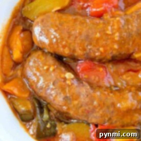 Crockpot sausage simmered in a tomato-based sauce with vibrant red and yellow bell peppers, served in a white bowl.