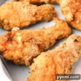 Four pieces of crispy fried chicken on a white plate, capturing the essence of a copycat Kentucky Fried Chicken recipe.