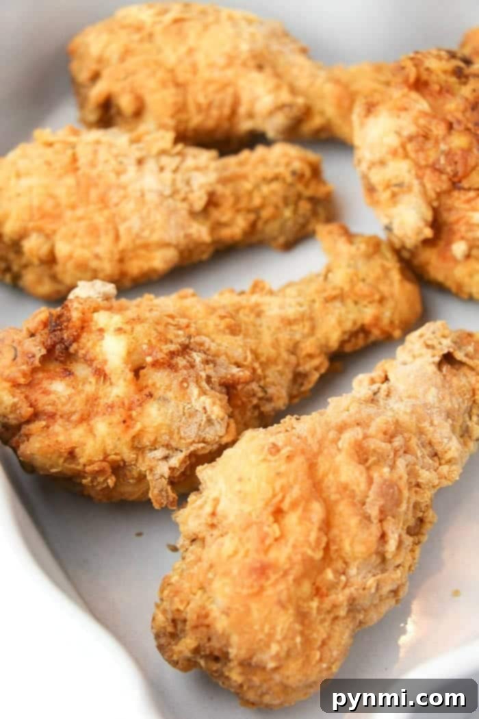 Easy copycat Kentucky Fried Chicken recipe for the crispiest chicken ever. Juicy chicken drumsticks fried quickly then baked to perfection & so flavorful. #kfc #kentuckyfriedchicken #copycat #friedchicken Enjoy four pieces of crispy fried chicken on a white plate, crafted with our special copycat Kentucky Fried Chicken recipe.