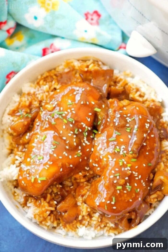 This easy crockpot sticky teriyaki chicken with a kick of heat recipe is amazing and a healthy meal too! Sweet with just a pinch of Sriracha makes it great! A vibrant bowl of rice topped with succulent crockpot teriyaki chicken, garnished with fresh chopped herbs, toasted sesame seeds, and drizzled with a rich brown teriyaki sauce, ready to be enjoyed.