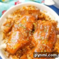 A beautifully presented bowl of rice topped with slow cooker teriyaki chicken, garnished with sesame seeds and green onions, resting on a blue surface with a floral napkin nearby.