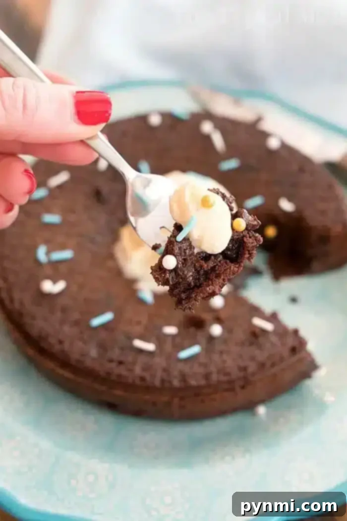 A person with red nail polish holds a spoonful of frosted chocolate cake, freshly baked in a pressure cooker, above a plate containing the remaining cake. Decorated with white and blue sprinkles, the cake has a slice missing, highlighting its moist interior.