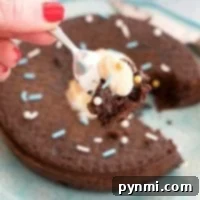 A hand with red nails holds a fork poised over a blue plate, ready to indulge in an instant pot chocolate pudding cake adorned with luscious frosting.
