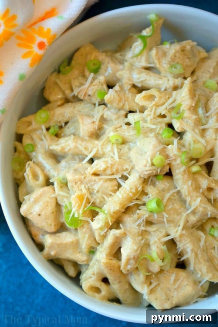 Cooked crockpot pesto chicken alfredo casserole with a serving spoon, garnished with fresh herbs