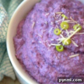 Creamy purple mashed cauliflower in a bowl, garnished with sliced green onions and grated cheese.