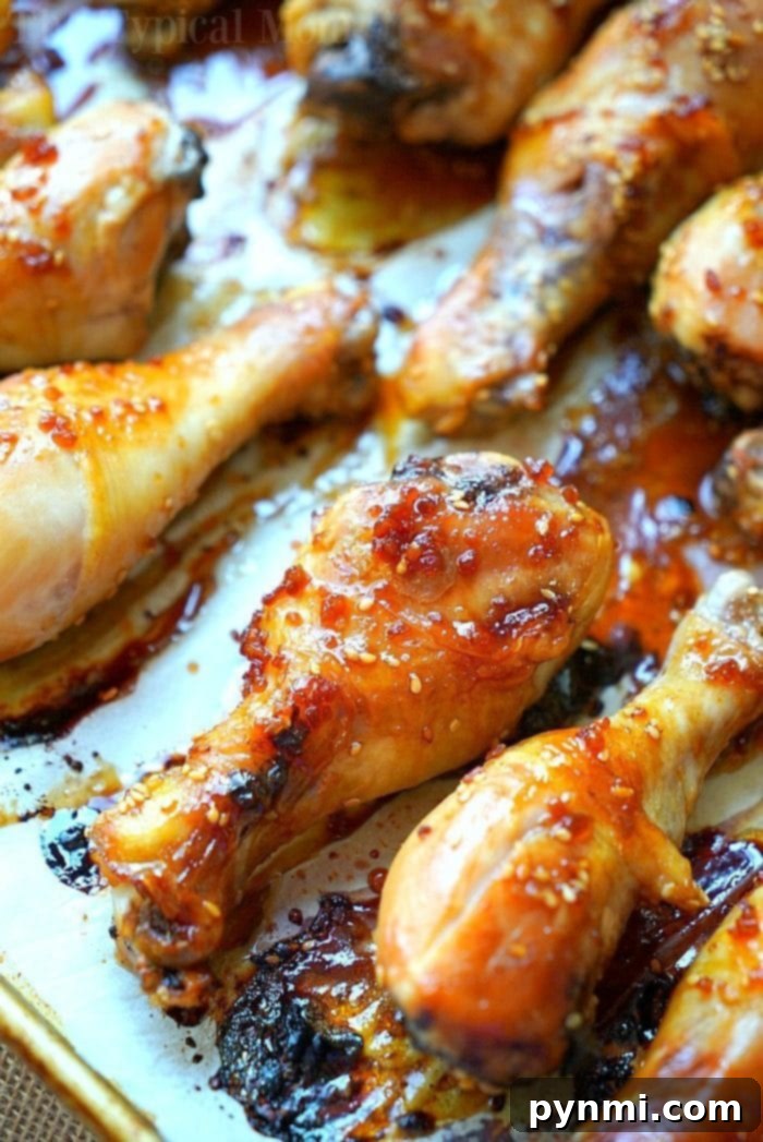 Baked teriyaki chicken drumsticks with an easy homemade sweet and spicy sauce you'll love! Moist chicken legs cooked in the oven in just about an hour. #baked #teriyaki #chicken #drumsticks #legs Close-up of teriyaki chicken drumsticks glazed with a sticky sauce, arranged on a baking tray. The drumsticks boast a golden-brown, crispy exterior with visible sesame seeds and caramelized edges, ready to be served.