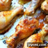 Close-up of teriyaki chicken drumsticks glazed with a sticky sauce, arranged on a baking tray. The drumsticks boast a golden-brown, crispy exterior with visible sesame seeds and caramelized edges.