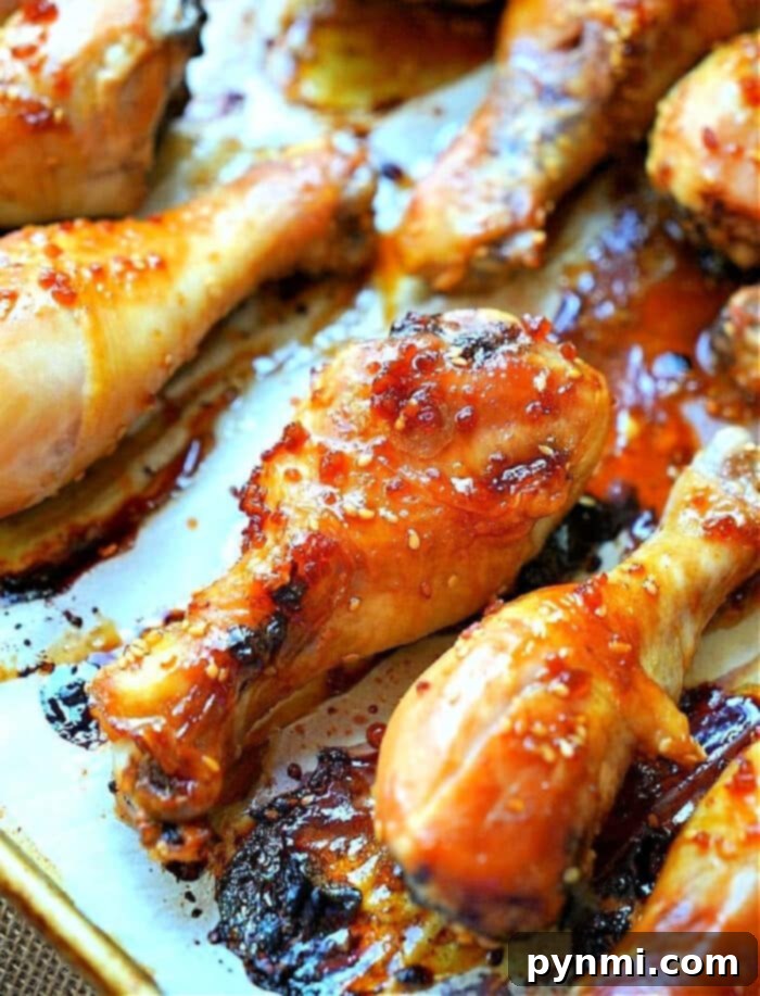 Sweet and Sticky Teriyaki Drumsticks 5 Close-up of roasted teriyaki chicken drumsticks, coated with a glossy, caramelized glaze and sprinkled with coarse salt. They rest on a parchment-lined baking sheet, showcasing their browned and crispy edges, fresh out of the oven.