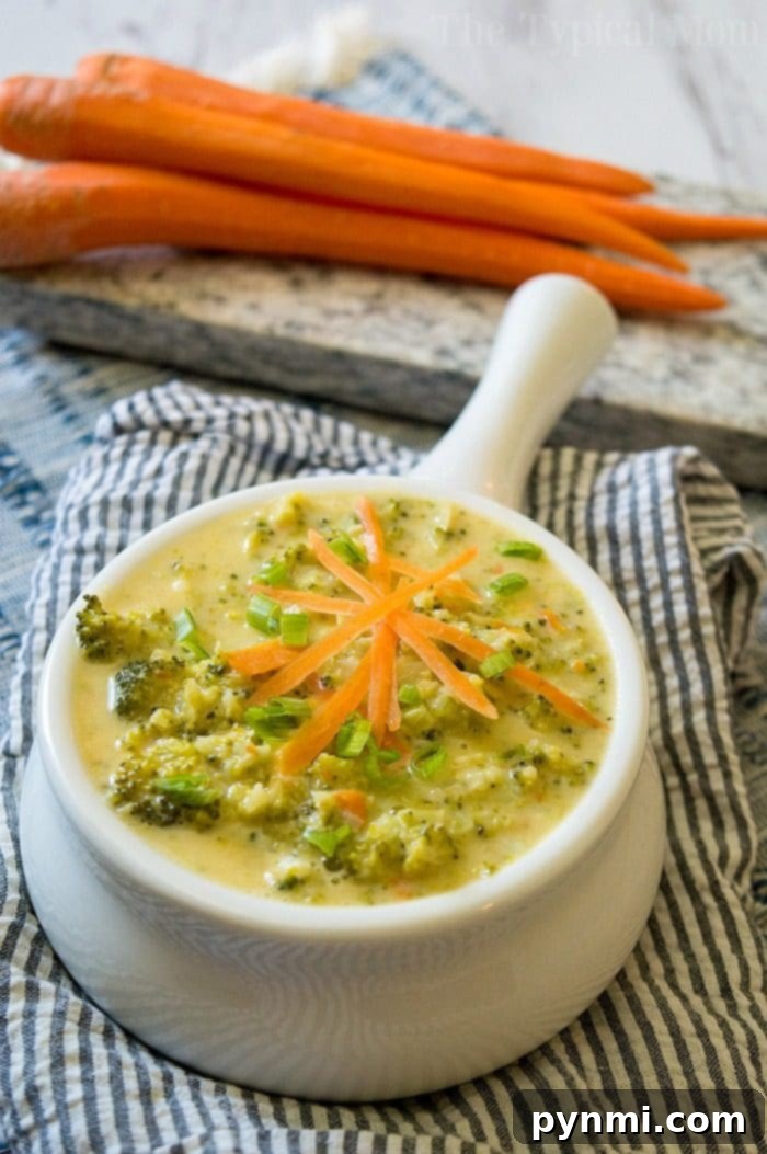A steaming bowl of quick broccoli cheese soup, garnished with fresh shredded carrots and green onions, served on a cozy striped cloth, perfect for a winter evening.