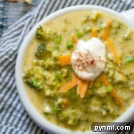 Bowl of quick broccoli cheese soup topped with shredded carrots, green onions, and a dollop of sour cream on a striped cloth.