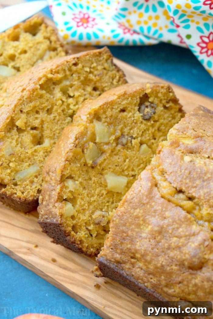 Harvest Spice Pumpkin Apple Bread 3 Slices of moist pumpkin apple bread with visible walnuts, elegantly arranged on a rustic wooden board with a festive floral cloth.