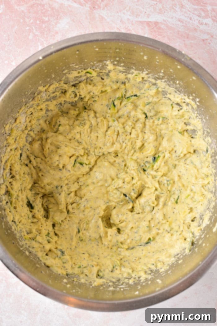 A vibrant yellow mixing bowl holds a creamy lemon poppy seed cake batter, ready for the Instant Pot, on a cheerful pink countertop.