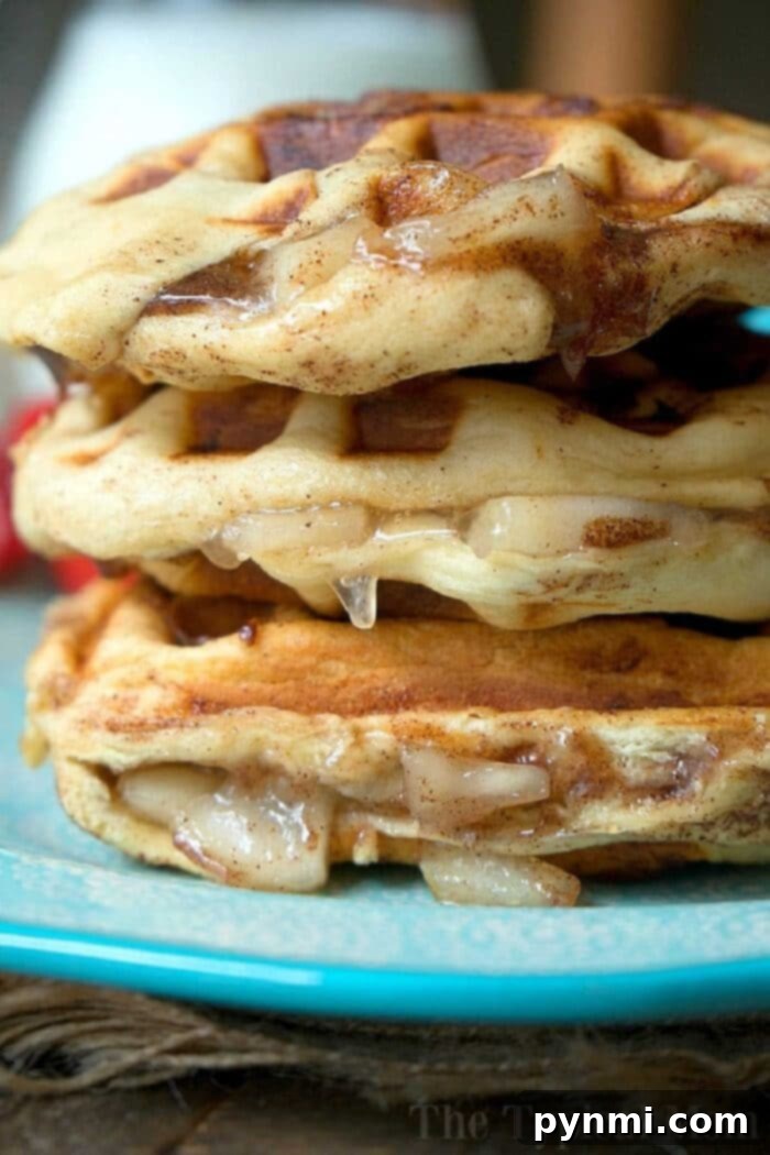 A close-up view of a stack of cinnamon roll waffles, glistening with syrup and icing, presented on a blue plate. This image perfectly captures the indulgent and tempting essence of cinnamon roll-inspired flavors in waffle form.