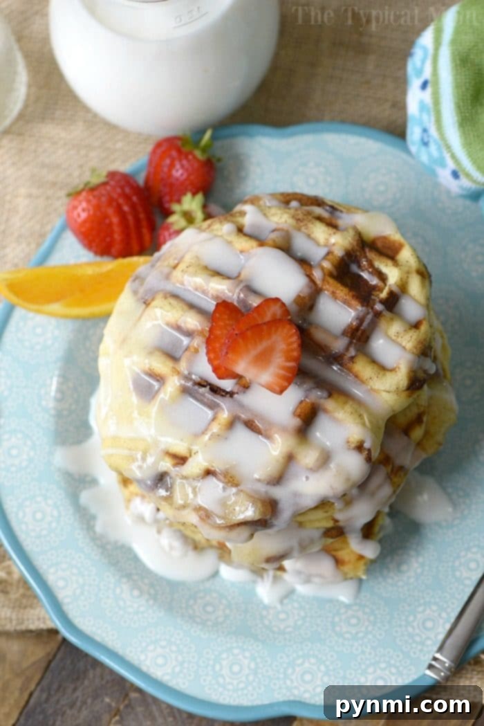 A delectable close-up of a stack of three glazed apple pie stuffed cinnamon roll waffles on a vibrant blue plate. The golden-brown, slightly crispy texture is evident, with sweet glaze gently dripping down. The background is softly blurred, focusing entirely on these irresistible breakfast or dessert treats. The watermark 'The Typical Mom' is subtly visible in the corner.