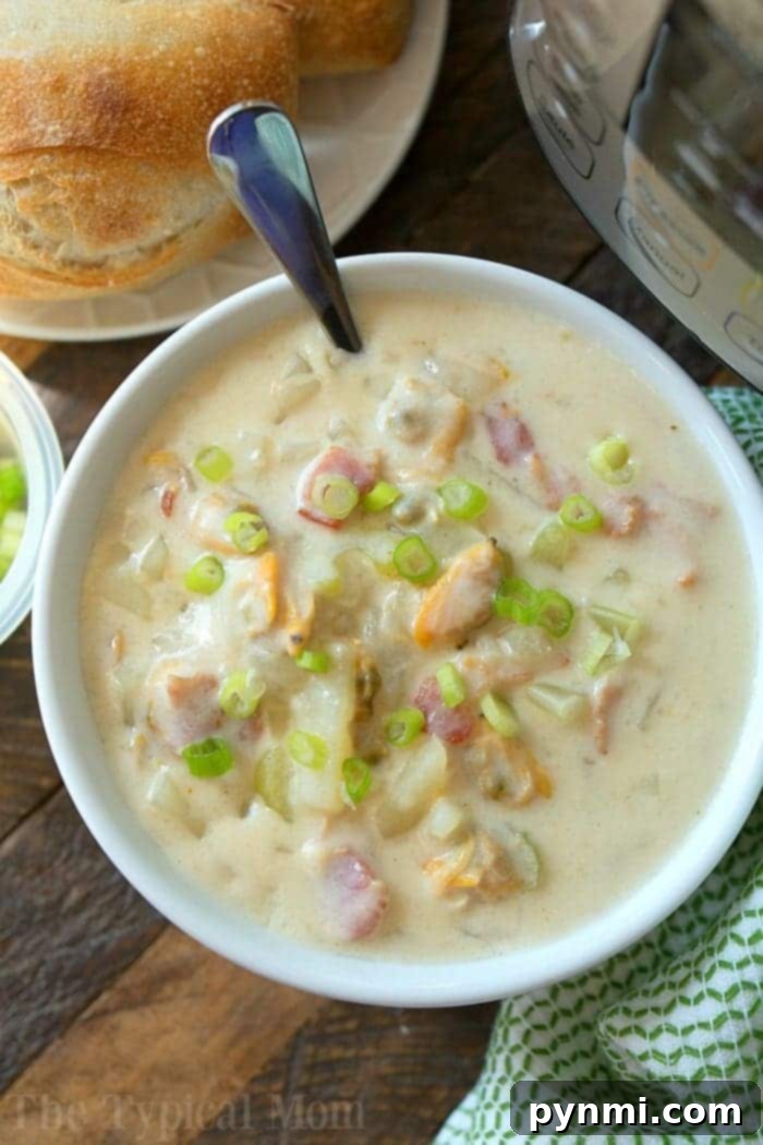 Instant Pot clam chowder soup recipe is packed with bacon and potatoes! One of the best pressure cooker soups I've made yet in just 10 minutes and it tastes just like Boudin Bakery's in San Francisco! Creamy and delicious dinner that my kids rave about and there are never leftovers. #instantpot #soup #clamchowder #pressurecooker #clam #chowder #thetypicalmom #instantpotrecipes A bowl of creamy clam chowder, made effortlessly as easy instant pot clam chowder, is garnished with chopped green onions on a wooden table. Beside it sits a loaf of bread and the partially visible pressure cooker. A green and white cloth peeks out next to the bowl.