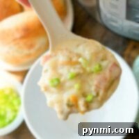 A ladle of creamy, easy Instant Pot clam chowder with diced vegetables is topped with chopped green onions. It's held above a white bowl, while an Instant Pot sits in the background alongside rolls and a small bowl of green onions on the wooden table.