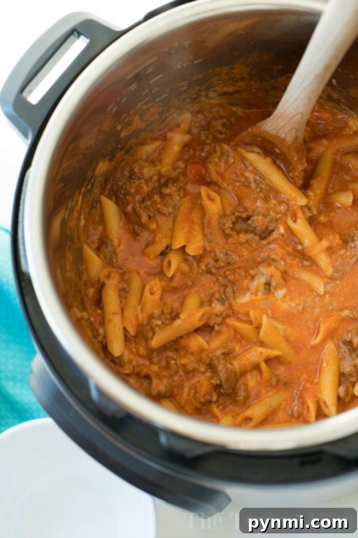 Easy Pressure Cooker lasagna casserole recipe our whole family loves. Cheesy Instant Pot lasagna but in a casserole which makes it much easier to make! #instantpot #lasagna #casserole #pressurecooker #instantpotrecipes #thetypicalmom Pressure cooker lazy lasagna stirred with a wooden spoon, blending layers of pasta and savory meat sauce.