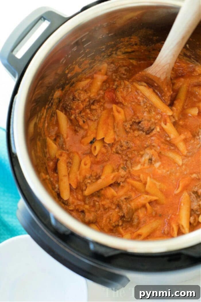 One-Pot Pressure Cooker Lasagna 4 Pasta with meat sauce being stirred with a wooden spoon inside an Instant Pot for a delicious pressure cooker lasagna casserole.
