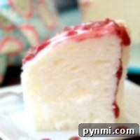 A slice of fluffy Instant Pot angel food cake topped with strawberry glaze sits elegantly on a white plate.