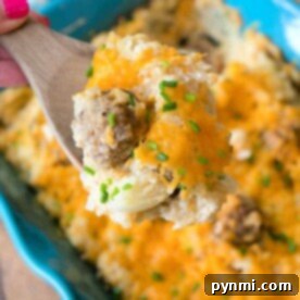 A wooden spoon holds a cheesy ground beef and hashbrown blend over a blue baking dish, reminiscent of a comforting hamburger hashbrown casserole with sour cream.