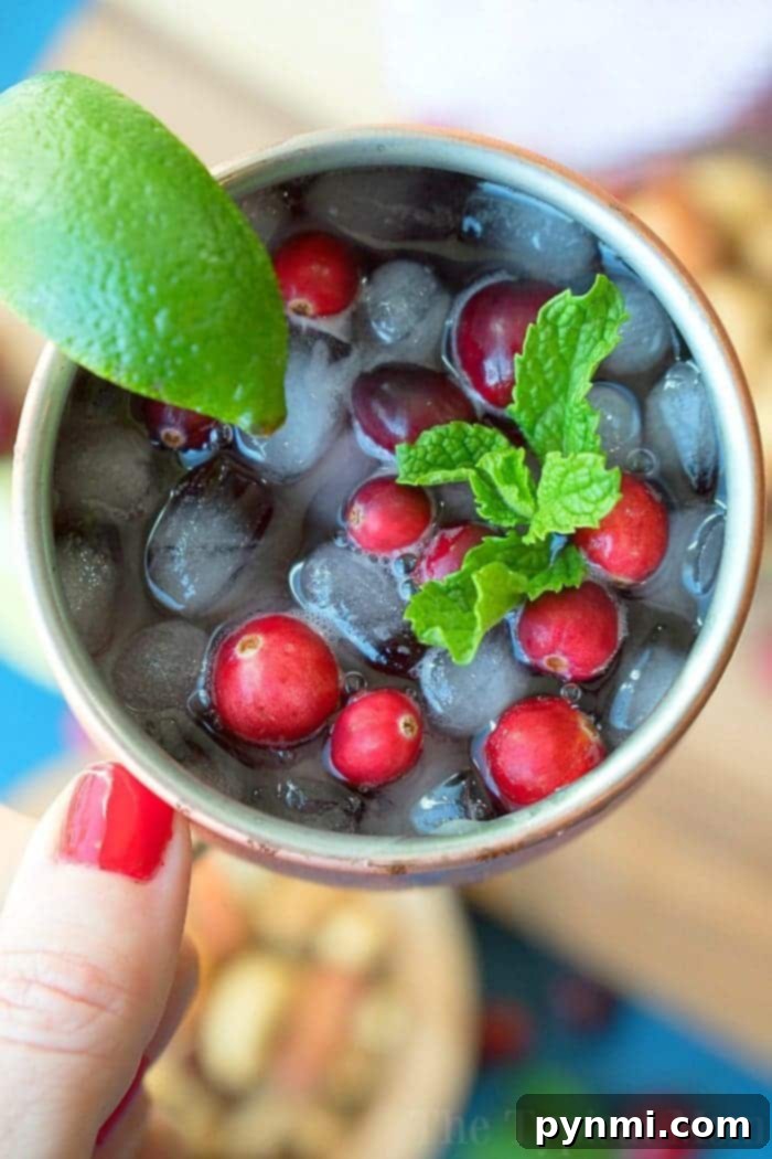 Festive Cranberry Moscow Mule: The Perfect Holiday Cocktail & Mocktail. Vibrant Cranberry Moscow Mule garnished with fresh cranberries, lime, and mint, in a copper mug.
