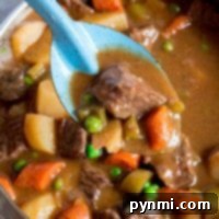 Close-up of a ladle lifting beef stew, simmered on high in a crockpot, with carrots, potatoes, peas, and celery from the pot.