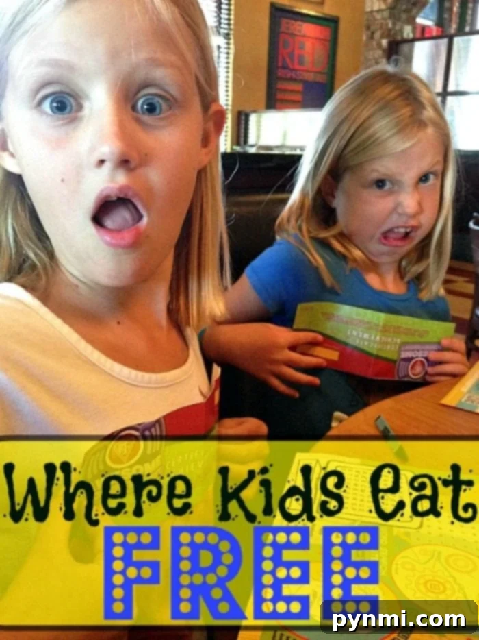 Two young girls with joyful expressions sit at a table in a bustling restaurant. One is dressed in a crisp white shirt, while the other sports a cheerful blue one. A yellow banner below proudly announces this as the place where kids eat free, adding to their excitement about the complimentary meal.