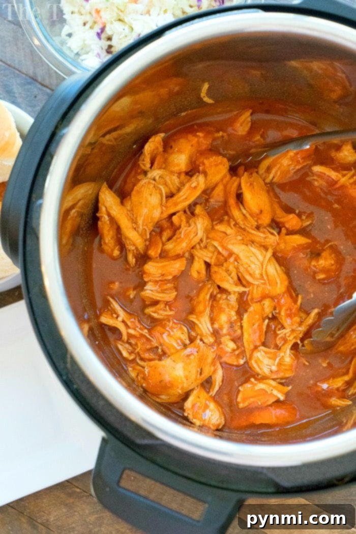 Close-up of shredded buffalo chicken in a pressure cooker, ready to be served on sliders.