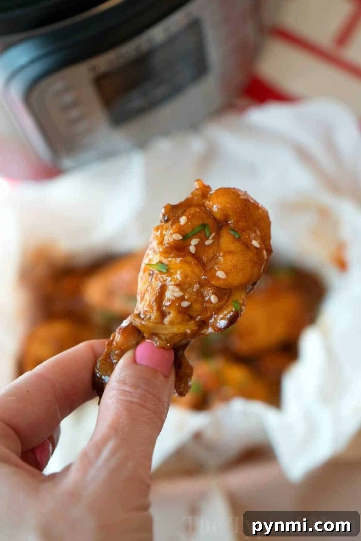 No Thawing Needed Pressure Cooker Wings 2 A hand holds a saucy chicken wing, topped with sesame seeds and herbs—perfect inspiration for making juicy pressure cooker frozen chicken wings at home.