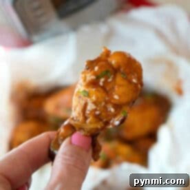 A hand holds a saucy chicken wing, topped with sesame seeds and herbs—perfect inspiration for making juicy pressure cooker frozen chicken wings at home.