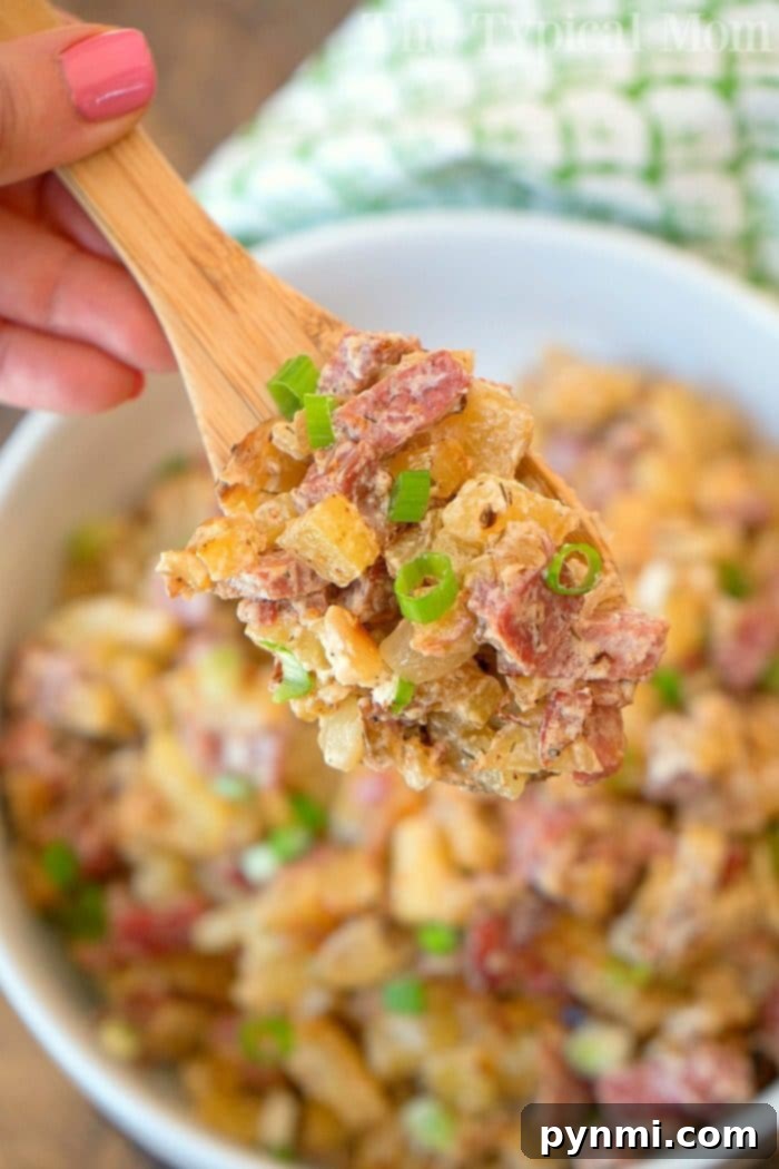 Homemade corned beef hash recipe! The traditional way which is a great hearty breakfast as well as a creamy corned beef hash that my family loves! It's a great way to use leftover corned beef after St. Patricks Day or any time of year. #cornedbeef #cornedbeefhash #homemade #stpatricksday #traditional Close-up of a wooden spoon with creamy corned beef hash garnished with green onions, perfect alongside your favorite homemade corned beef hash recipe.