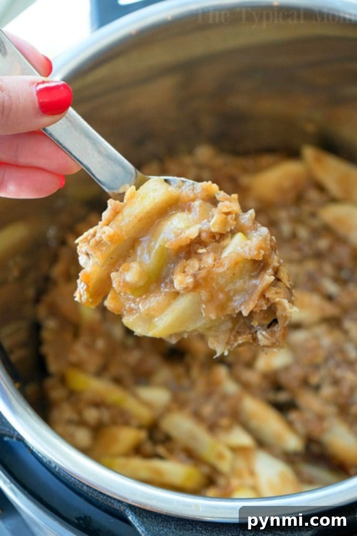 Instant Pot apple crisp recipe is amazing! Tastes like copycat Cracker Barrel baked apples we love but made in less than 20 minutes total. Warm cinnamon apples coated with a ooey gooey brown sugar glaze your family will go crazy over for sure. Try this homemade pressure cooker fruit dessert this week! #instantpot #pressurecooker #apples #applecrisp #dessert #bakedapples #instantpotrecipes #thetypicalmom #easy A hand holding a spoonful of crumbly apple crisp over an Instant Pot filled with delicious apple crisp.