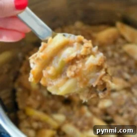 A hand holding a spoonful of delicious instant pot apple crisp from a pot.